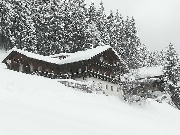 A snow-covered lodge with a prominent central structure, surrounded by dense forest.