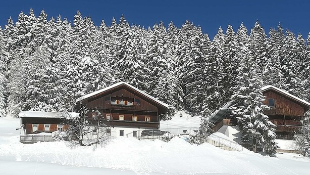 A snow-covered lodge with multiple wooden cabins, surrounded by dense evergreen trees. - Wohnung Ost - Haus Lukasser (Kosten)