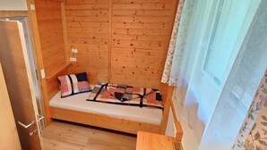 A small wooden room with a bunk bed, a door, and a window with floral curtains. - Wohnung Ost - Haus Lukasser (Kosten)