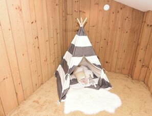 Una habitación de madera con una estructura parecida a una tienda de rayas, un objeto blanco y mullido, y un objeto pequeño y blanco en el suelo.