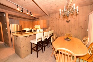 Interior de una cabaña de madera con cocina, comedor y una araña.