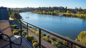Un balcon donnant sur une rivière, entouré de verdure et avec des bâtiments en arrière-plan.