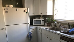 Une cuisine de taille réduite avec des meubles blancs, un réfrigérateur, un four à micro-ondes et un évier.