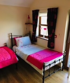 A small, single-bed room with a wooden floor, a window with curtains, and a bedside table.