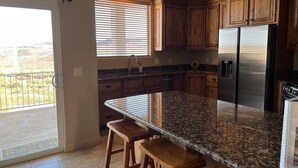 A kitchen with wooden cabinets, a stainless steel refrigerator, granite countertops, and a window with blinds. - "Desert Blossom"- Exceptionally Relaxing Vacation Destination! (St. George)