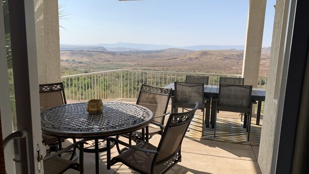 A covered patio with a round table and chairs, offering a view of distant hills. - "Desert Blossom"- Exceptionally Relaxing Vacation Destination! (St. George)