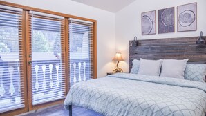 Un dormitorio con cama, mesita de noche, lámpara y vistas al exterior a través de una puerta corredera.