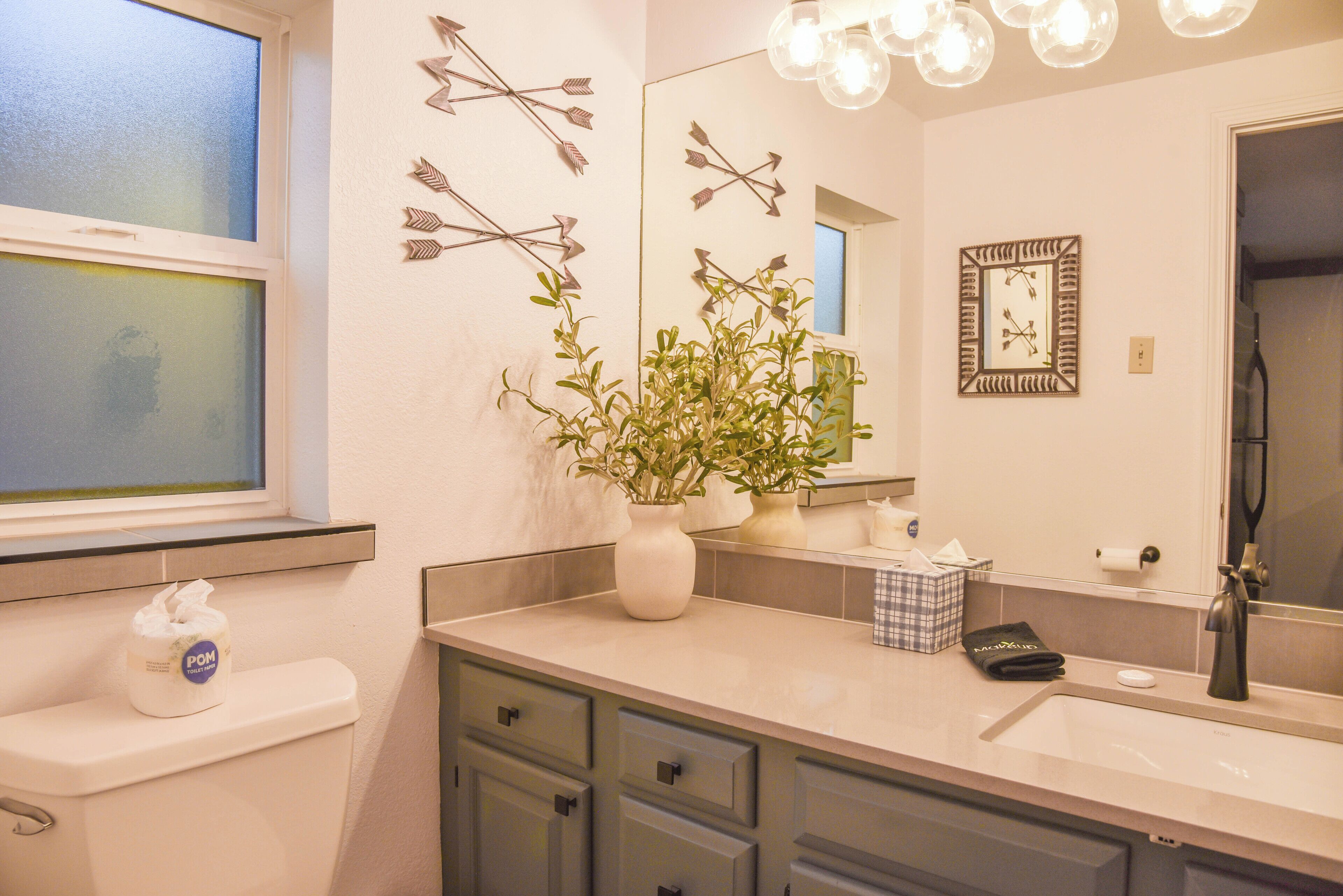 A bathroom with a toilet, sink, mirror, and decorative wall art.