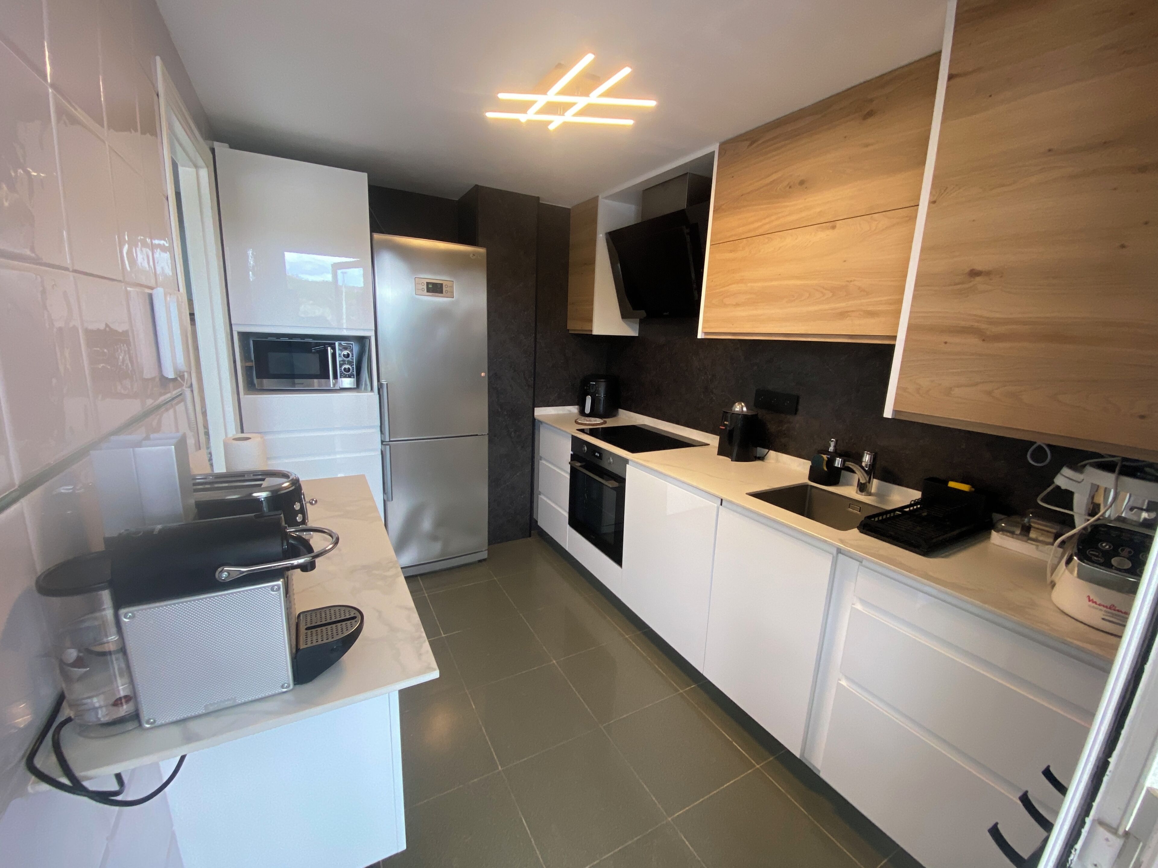 A modern kitchen with white cabinets, a stainless steel refrigerator, a microwave, a coffee maker, and a sink.