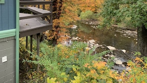 Une terrasse en bois donnant sur une rivière, avec le feuillage automnal en arrière-plan.