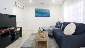 A modern living room with a flat-screen TV, a wooden coffee table, a blue sofa, and a large abstract painting on the wall. - Beautiful Waterfront Condo on Canal with Pool & Walk to Beach! Boat Watch! 2b/2b (Pompano Beach)