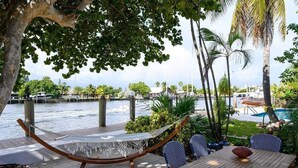 A hammock chair, dining table, and chairs by a waterfront with a pool and palm trees. - Beautiful Waterfront Condo on Canal with Pool & Walk to Beach! Boat Watch! 2b/2b (Pompano Beach)