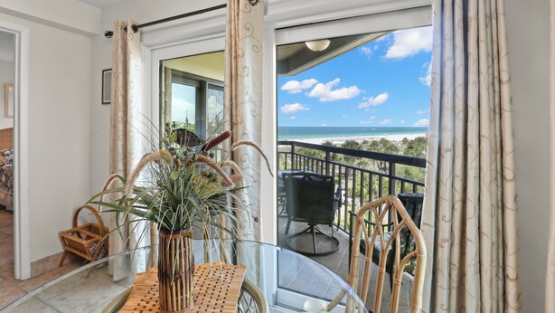 A balcony with a view of the beach, a glass table, wicker chairs, and a potted plant. - 🌿 Select View Condo — Gulf Strand Resort, St. Pete Beach (St Pete Beach)