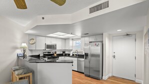 A modern kitchen with a central island, stainless steel appliances, and a dining area with a chair and table. - 🌿 Select View Condo — Gulf Strand Resort, St. Pete Beach (St Pete Beach)
