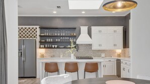 A modern kitchen with white cabinets, a central island with stools, and a dining table with a bowl.