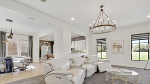A spacious living room with a sectional sofa, a glass coffee table, and a chandelier.