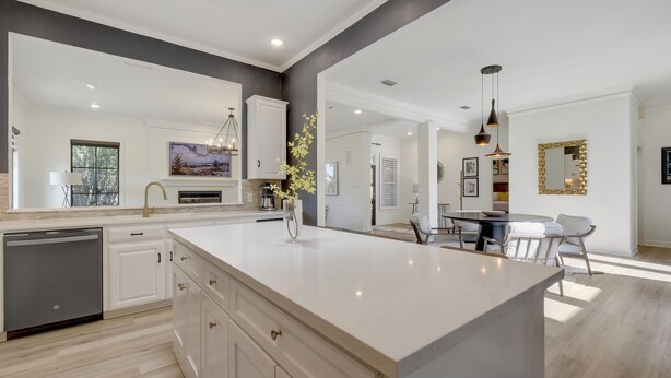 A modern kitchen with a large island, white cabinetry, and a dining area with a round table and chairs.
