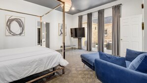 A modern bedroom with a four-poster bed, a flat-screen TV, and a blue sofa.