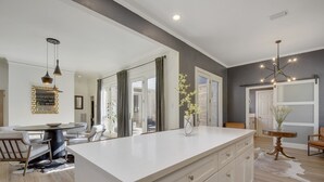 A modern kitchen with a large island, white cabinetry, and a dining area with a round table and chairs.