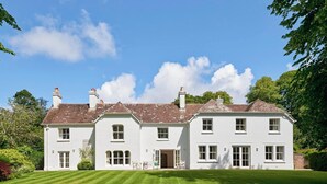 Un grand bâtiment blanc à deux étages, doté d’une façade symétrique, de nombreuses cheminées et d’une pelouse bien entretenue à l’avant.