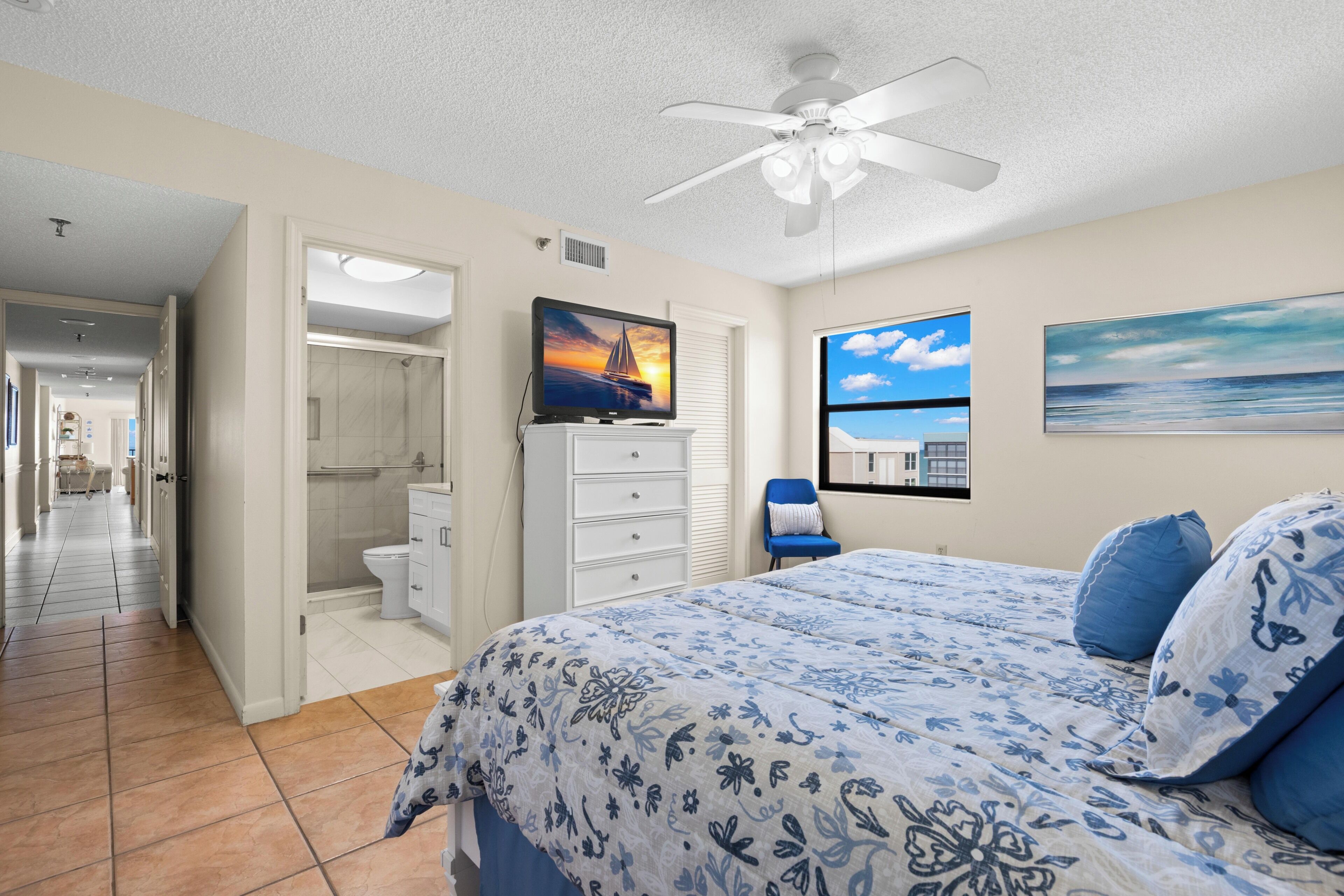 Un dormitorio con cama, ventilador de techo, televisor y baño con ducha, y vista al océano.