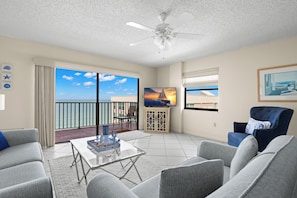 A living room with a balcony, a ceiling fan, a TV, and a painting.