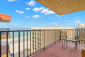 Un balcon avec vue sur la plage et l’océan, une table en verre et une chaise.