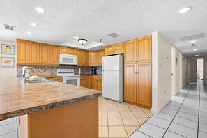 A kitchen with wooden cabinets, a granite countertop, a white refrigerator, and a microwave.
