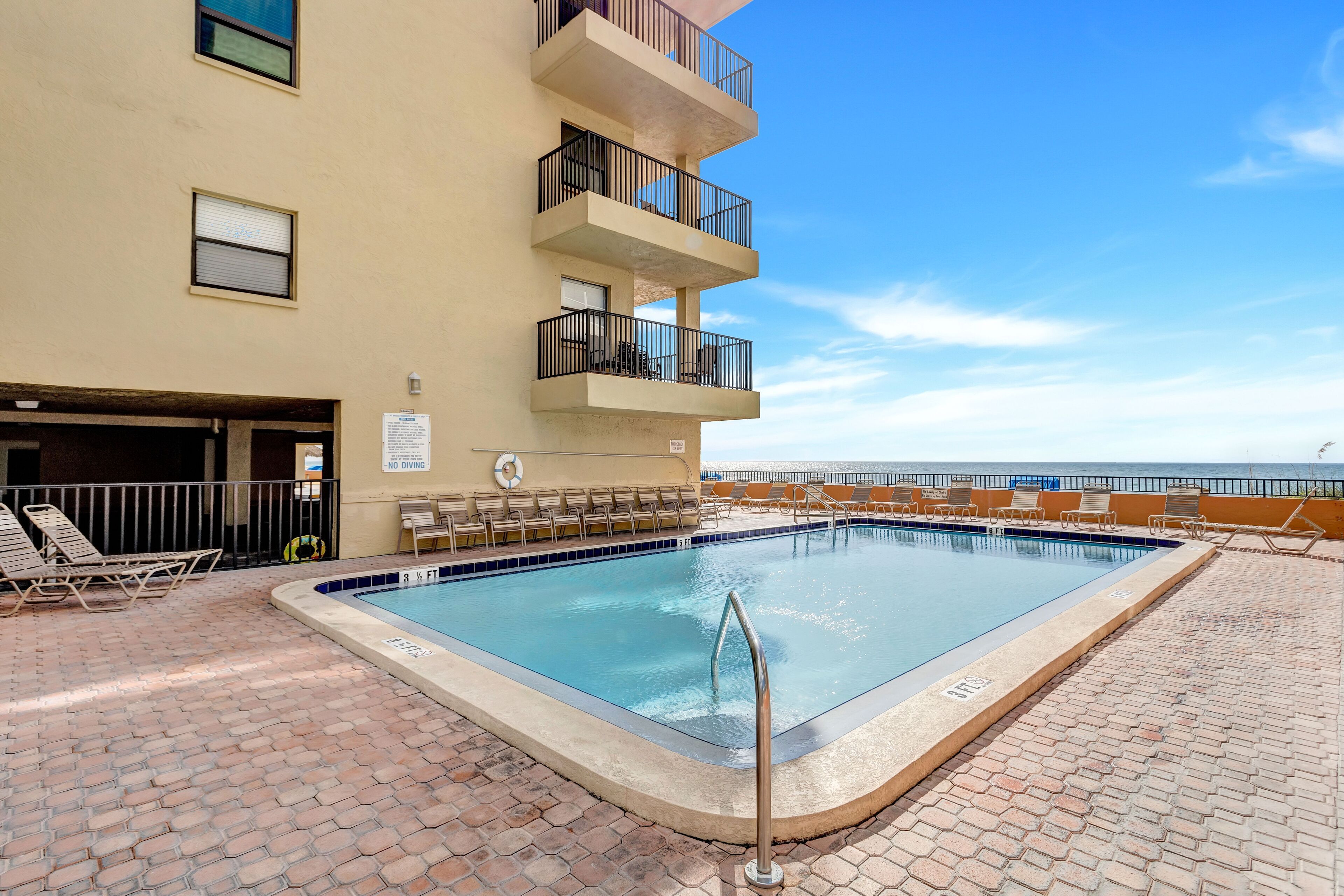 Une piscine avec des chaises longues et un panneau indiquant qu’il est interdit de plonger, le tout situé sur un bâtiment doté de balcons.