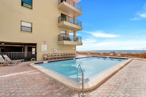 A swimming pool with lounge chairs, a lifeguard stand, and a view of the ocean.