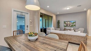 A modern living room with a wooden dining table, a sofa, and a TV mounted on the wall. - 5BD Windsor Westside Private Pool - WW 9025 (Kissimmee)