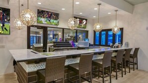 A modern kitchen with a long island, bar stools, pendant lighting, and sports-themed decor. - 5BD Windsor Westside Private Pool - WW 9025 (Kissimmee)