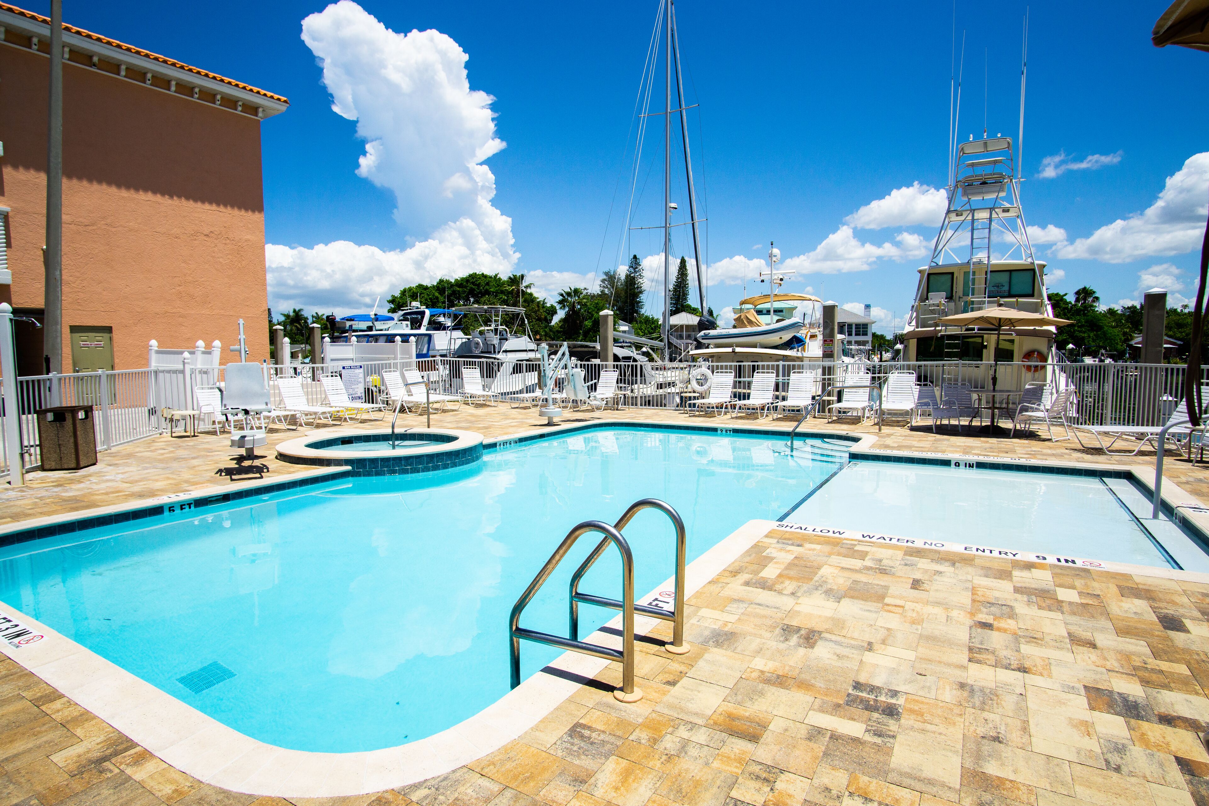 Une piscine avec un plongeoir, des chaises longues et un bateau amarré à proximité.
