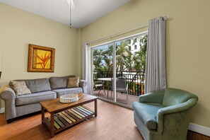 A living room with a sofa, a coffee table, and a chair. There is a large sliding glass door leading to an outdoor area with a balcony. - 🌞 Madeira Bay Resort II – Beachside Comfort with Balcony & Poolside Perks (Madeira Beach)
