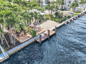 A waterfront property with a wooden deck, outdoor seating, and palm trees. - Beautiful & Spacious Waterfront Condo, Walk to the BEACH, On Canal, 2 bed/2 bath (Pompano Beach)