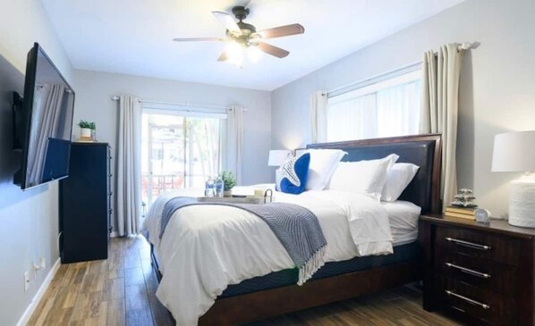 A hotel room with a bed, a ceiling fan, a TV mounted on the wall, and a window with curtains. - Beautiful & Spacious Waterfront Condo, Walk to the BEACH, On Canal, 2 bed/2 bath (Pompano Beach)