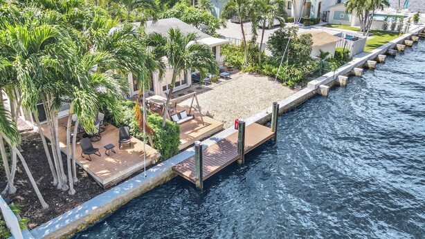 A waterfront property with a wooden deck, outdoor seating, and lush greenery. - Beautiful & Spacious Waterfront Condo, Walk to the BEACH, On Canal, 3 bed/2 bath (Pompano Beach)