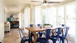 A dining area with a wooden table and blue chairs, a ceiling fan, and large windows with sheer curtains. - Beautiful & Spacious Waterfront Condo, Walk to the BEACH, On Canal, 3 bed/2 bath (Pompano Beach)