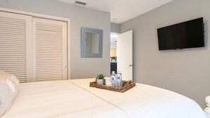A bedroom with a bed, a television, a mirror, and a door. - Beautiful & Spacious Waterfront Condo, Walk to the BEACH, On Canal, 3 bed/2 bath (Pompano Beach)