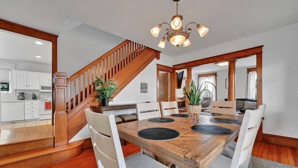 A dining area with a wooden table, white chairs, and a staircase leading to a kitchen. - Backyard Retreat (RONKS)