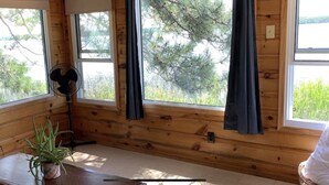 Una cabana amb grans finestres, un ventilador, una taula amb una planta i una cadira.