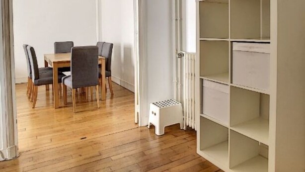 Una habitación con piso de madera, una mesa de comedor con sillas y un estante blanco.
