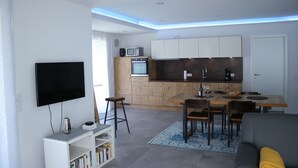 A modern kitchen with wooden cabinets, a built-in oven, and a microwave. There is a dining area with a table and chairs, and a flat-screen TV mounted on the wall. - die Fewo im Herzen der Pfalz (Lug)