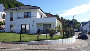 A modern two-story house with a balcony, a fenced garden, and a paved driveway. - die Fewo im Herzen der Pfalz (Lug)
