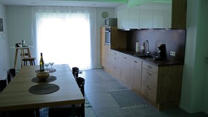 A modern kitchen with wooden cabinets, a built-in oven, and a microwave. There is a dining table with a bottle and glasses on it. - die Fewo im Herzen der Pfalz (Lug)