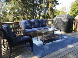 Eine Terrasse mit einem blauen Sofa, Korbstühlen und einem Grill.