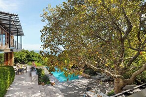 Zona de piscina con cubierta de madera, sillas de descanso y pérgola.