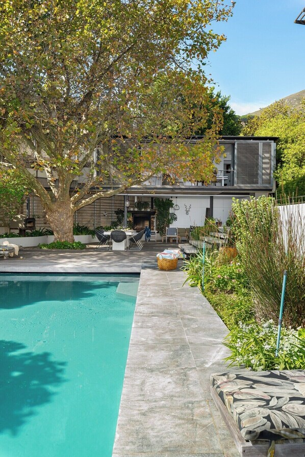 A modern house with a swimming pool, outdoor furniture, and a large tree.