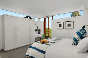 A modern bedroom with a large bed, a wardrobe, and a window with a view of trees.