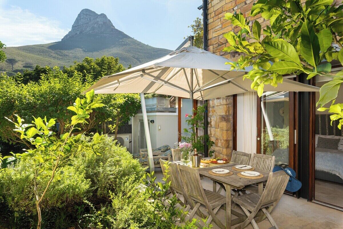 An outdoor dining area with a table and chairs, a large umbrella, and a mountain view in the background.